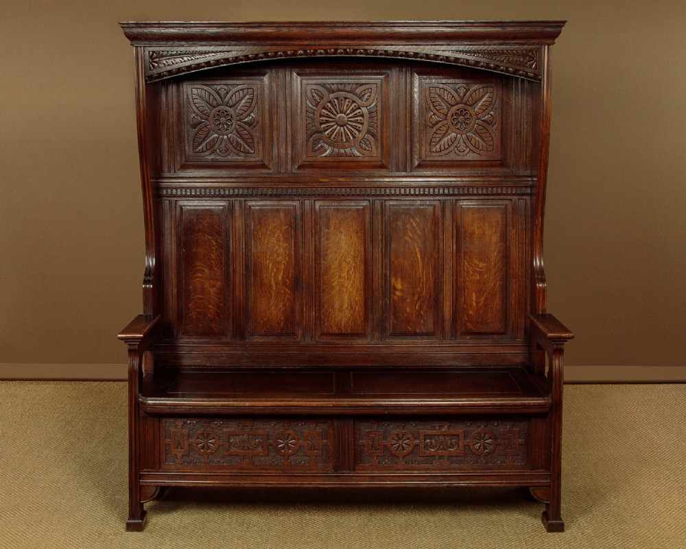 A dark oak canopy box settle featuring intricate carved floral panels, a tall fielded-panel back, and a lift-up storage seat base.