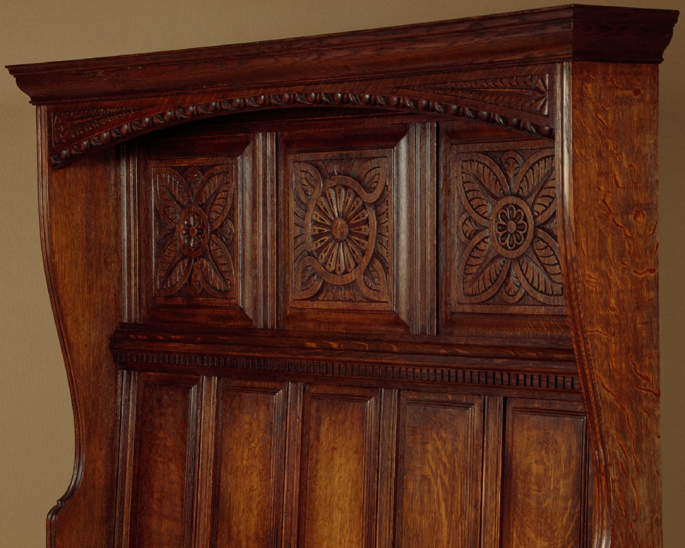 A dark oak canopy box settle featuring intricate carved floral panels, a tall fielded-panel back, and a lift-up storage seat base. View III