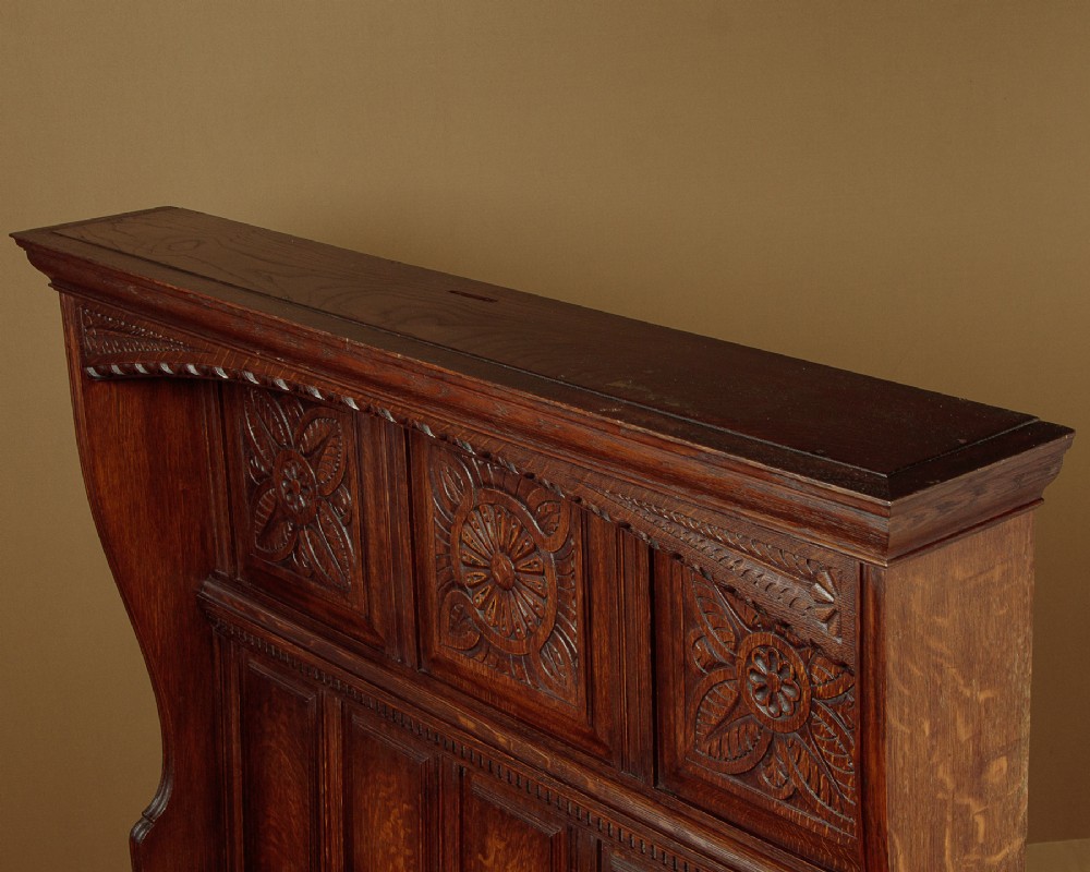 A dark oak canopy box settle featuring intricate carved floral panels, a tall fielded-panel back, and a lift-up storage seat base. View V