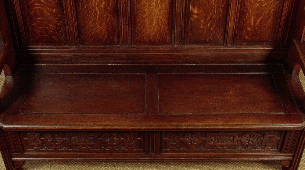 A dark oak canopy box settle featuring intricate carved floral panels, a tall fielded-panel back, and a lift-up storage seat base. View VI