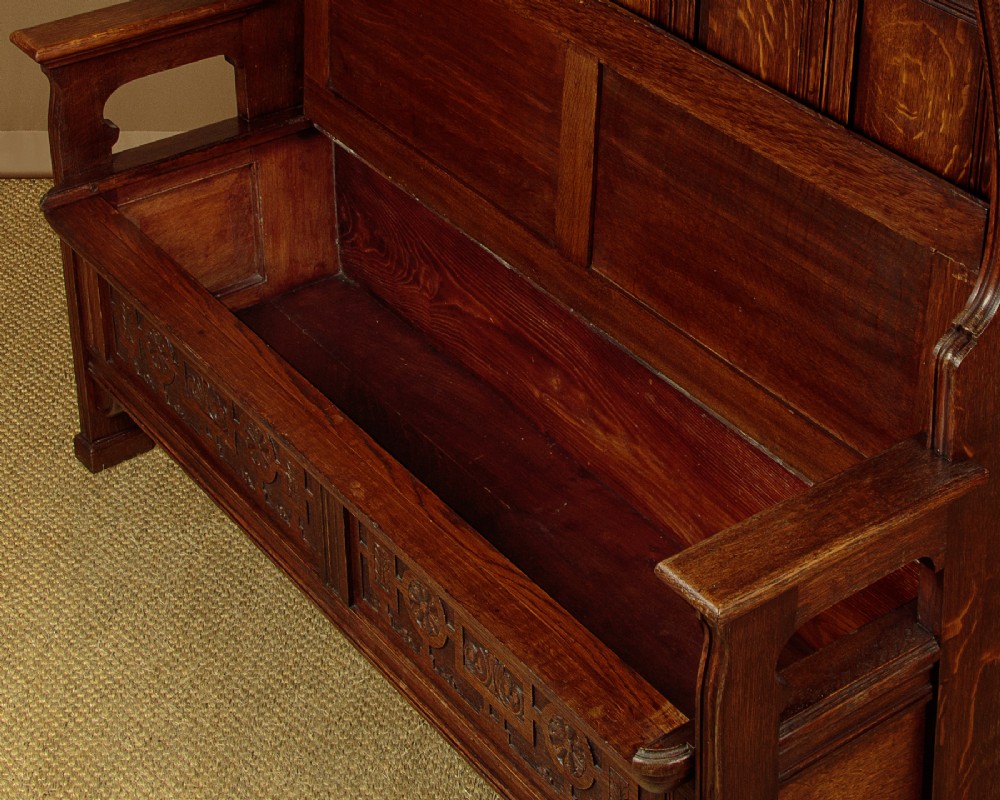 A dark oak canopy box settle featuring intricate carved floral panels, a tall fielded-panel back, and a lift-up storage seat base. View VII