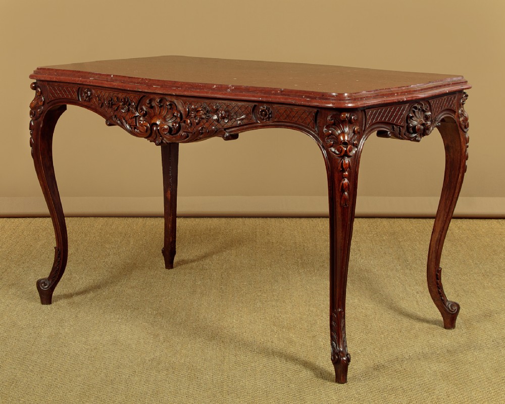 A late nineteenth-century carved walnut centre table with cabriole legs, Rococo frieze carving, and a rouge marble top.