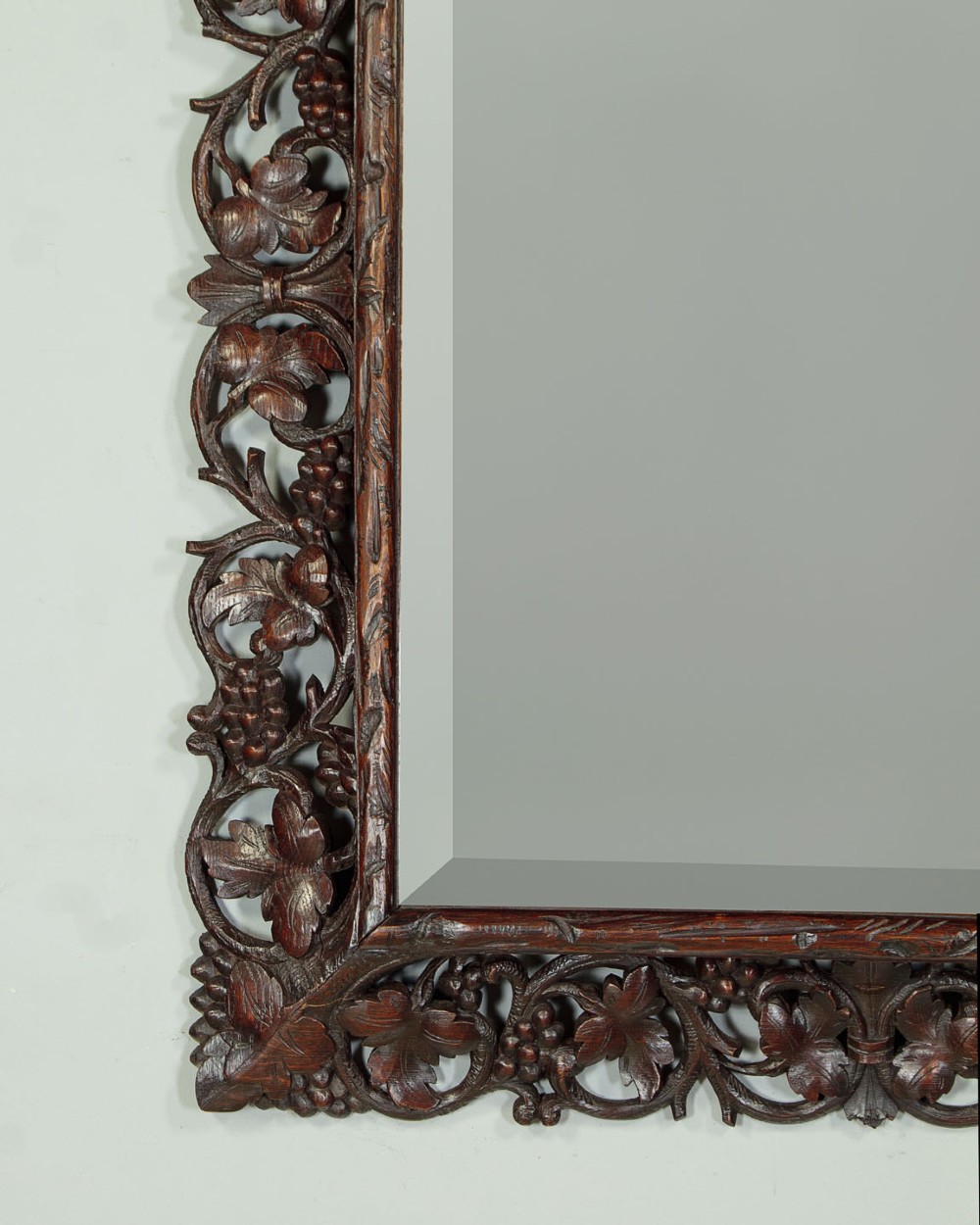 A rectangular dark oak wall mirror featuring intricate openwork carvings of grapevines and leaves framing a bevelled glass plate. View VI