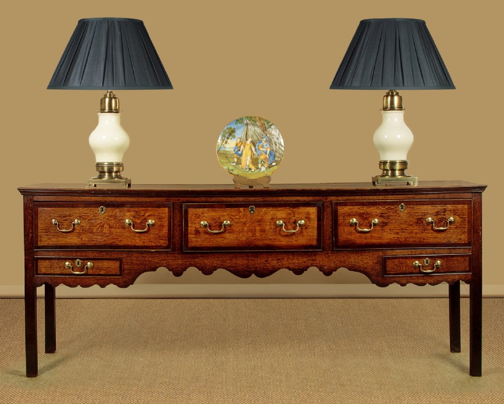 A long Georgian oak dresser base featuring five drawers with brass swan-neck handles, crossbanded drawer borders, a scalloped apron, and straight legs. View II