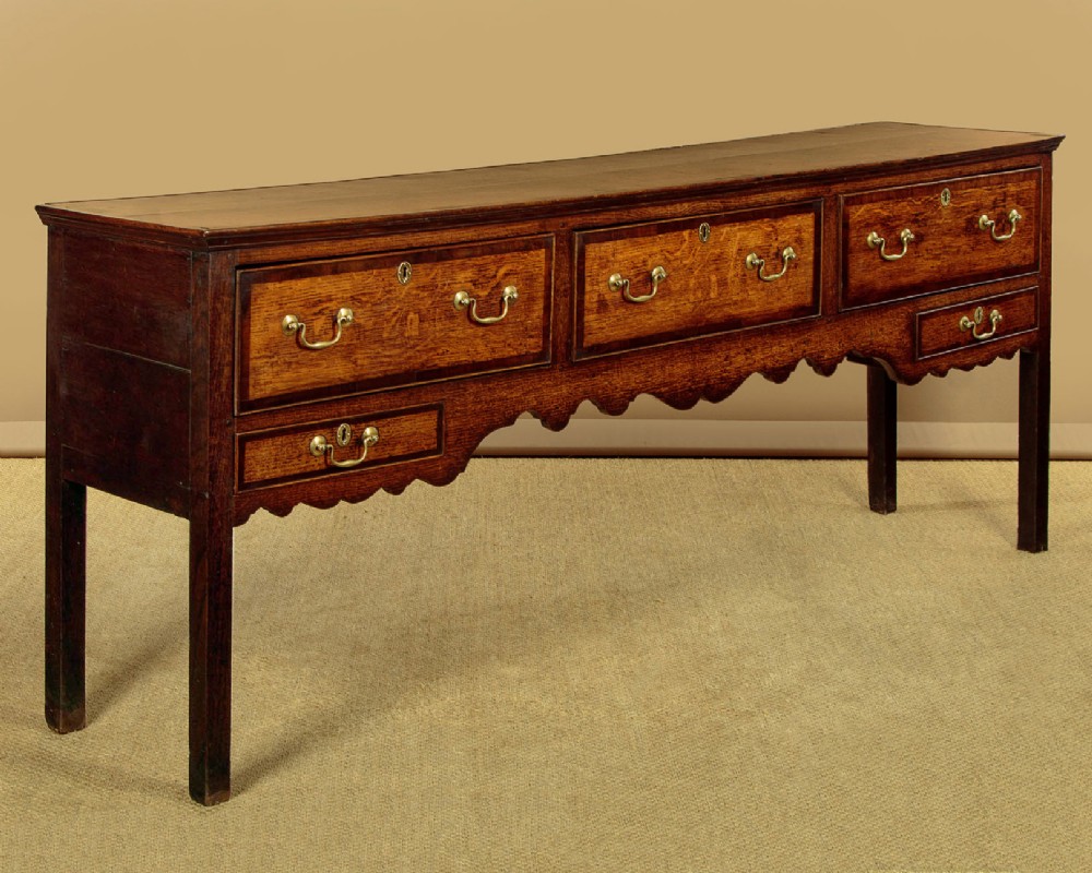 A long Georgian oak dresser base featuring five drawers with brass swan-neck handles, crossbanded drawer borders, a scalloped apron, and straight legs. View III