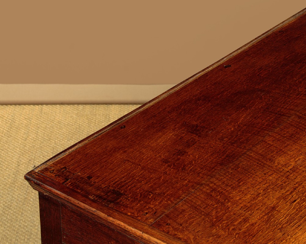 A long Georgian oak dresser base featuring five drawers with brass swan-neck handles, crossbanded drawer borders, a scalloped apron, and straight legs. View VII