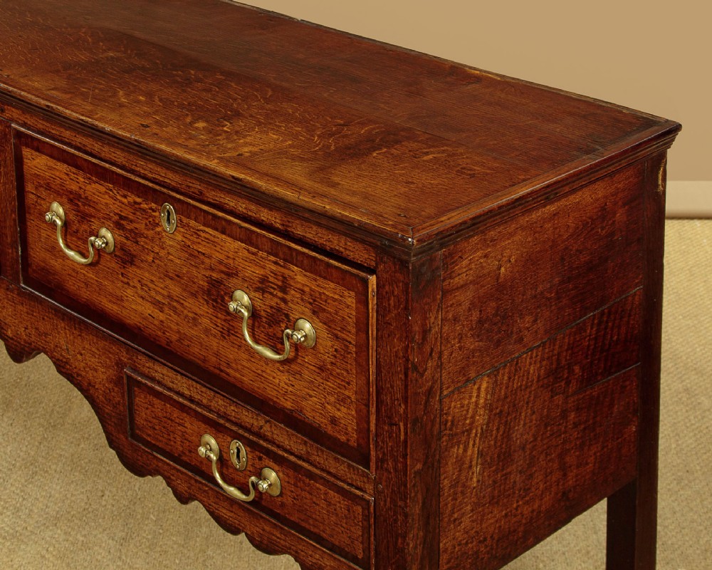 A long Georgian oak dresser base featuring five drawers with brass swan-neck handles, crossbanded drawer borders, a scalloped apron, and straight legs. View VIII