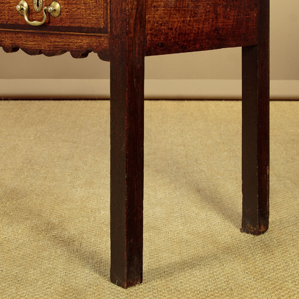 A long Georgian oak dresser base featuring five drawers with brass swan-neck handles, crossbanded drawer borders, a scalloped apron, and straight legs. View XII