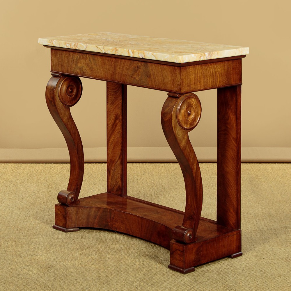 A late 19th-century mahogany console table featuring a light yellow marble top, S-scroll front supports with carved roundels, and a concave plinth base.