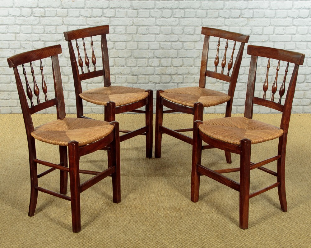 A set of four dark wood dining chairs featuring turned spindle backrests and hand-woven rush seats.