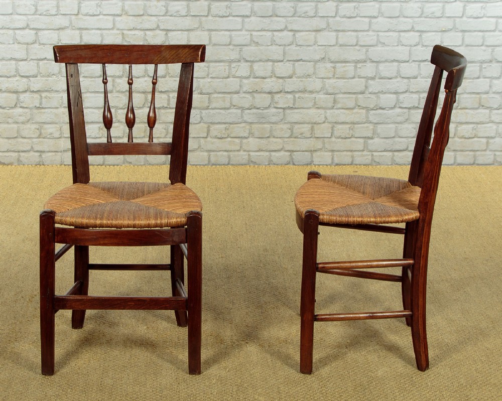 A set of four dark wood dining chairs featuring turned spindle backrests and hand-woven rush seats. View II