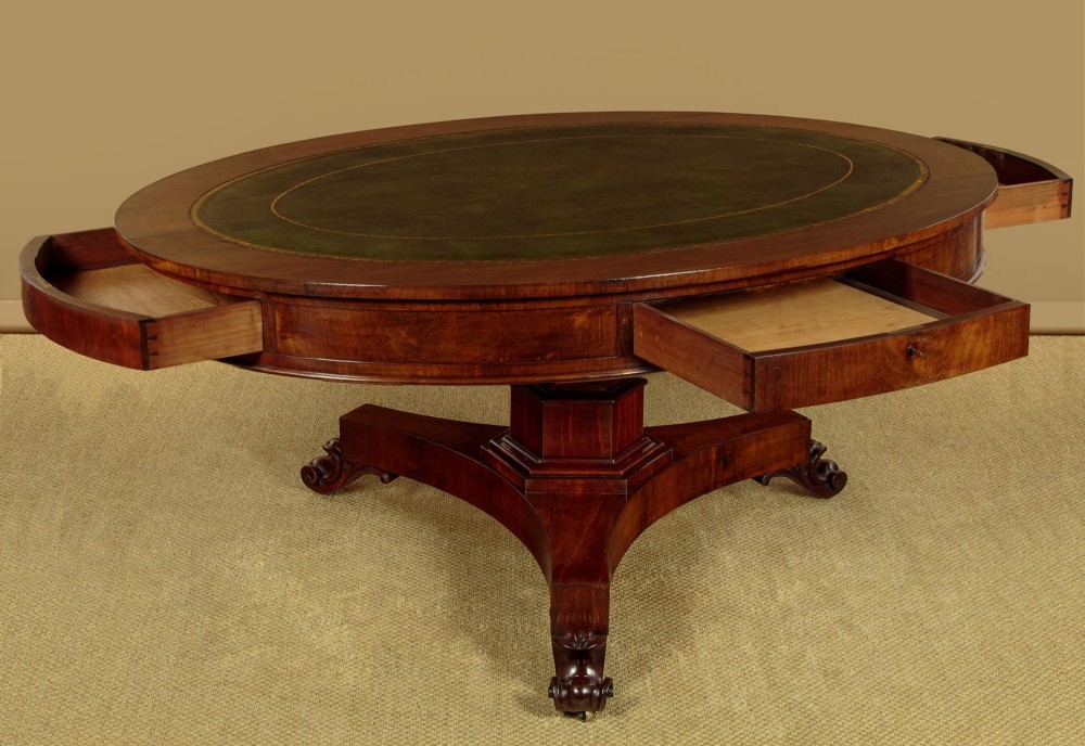 An oval Victorian mahogany library table featuring a green gilt-tooled leather top, frieze drawers, and a central pedestal with carved scroll feet on castors. View III