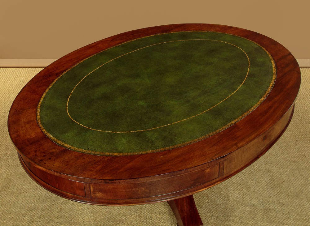 An oval Victorian mahogany library table featuring a green gilt-tooled leather top, frieze drawers, and a central pedestal with carved scroll feet on castors. View IV