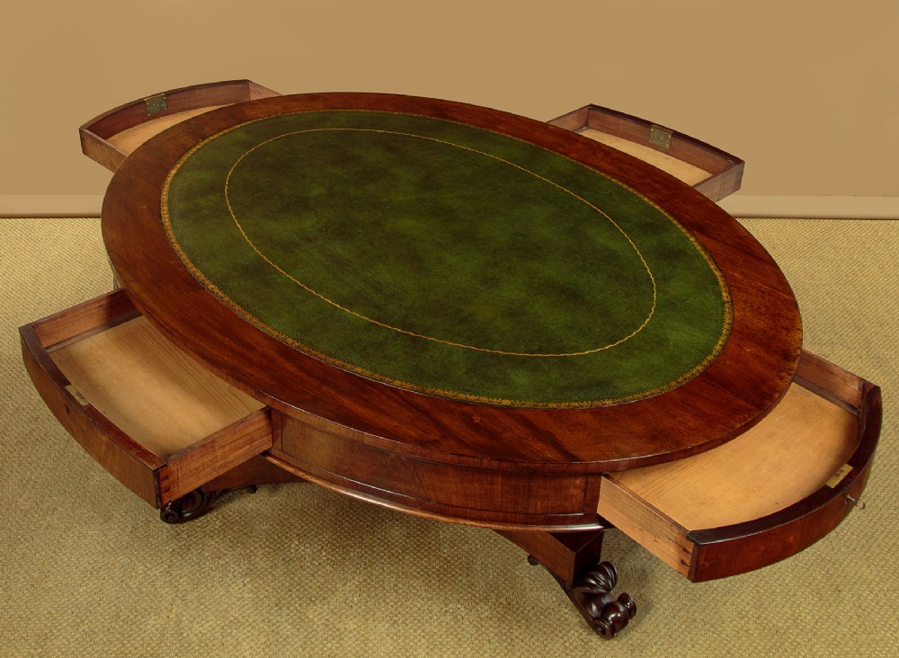 An oval Victorian mahogany library table featuring a green gilt-tooled leather top, frieze drawers, and a central pedestal with carved scroll feet on castors. View V