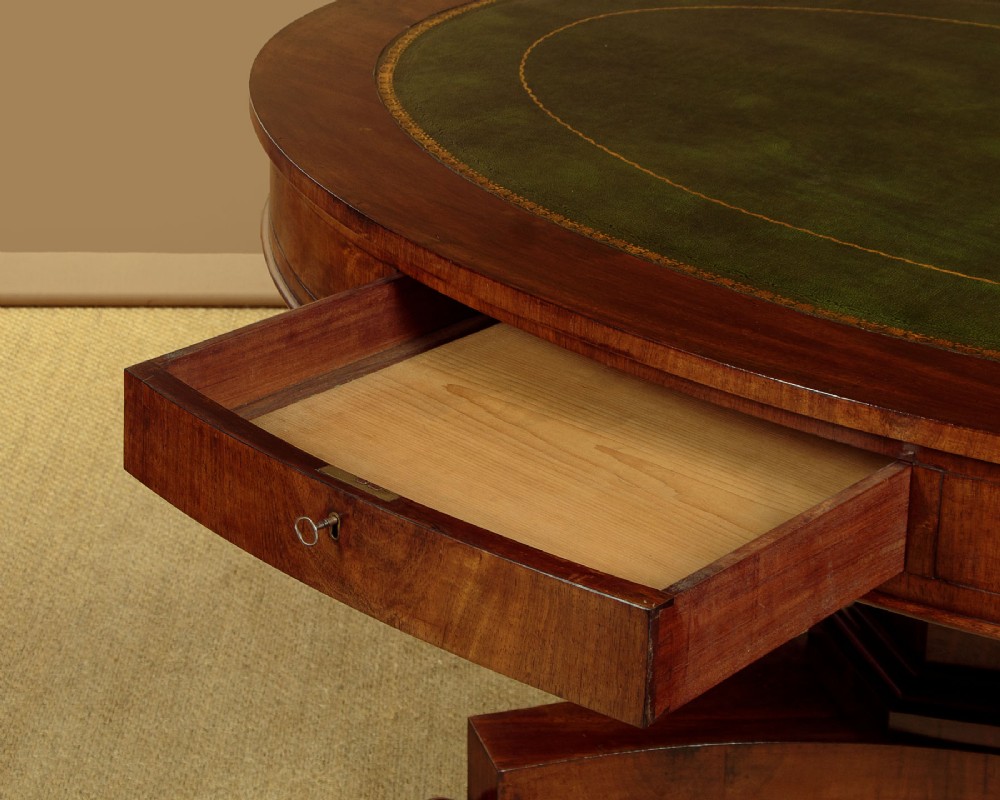 An oval Victorian mahogany library table featuring a green gilt-tooled leather top, frieze drawers, and a central pedestal with carved scroll feet on castors. View VI