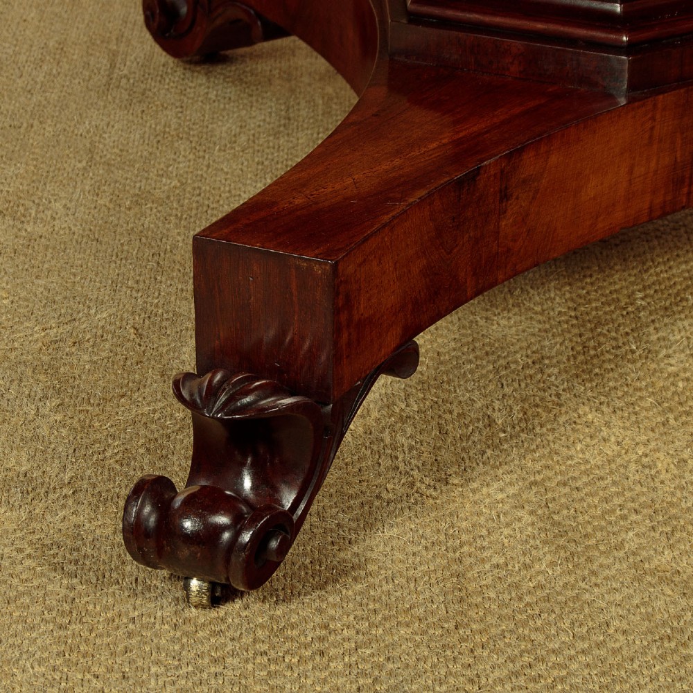 An oval Victorian mahogany library table featuring a green gilt-tooled leather top, frieze drawers, and a central pedestal with carved scroll feet on castors. View X