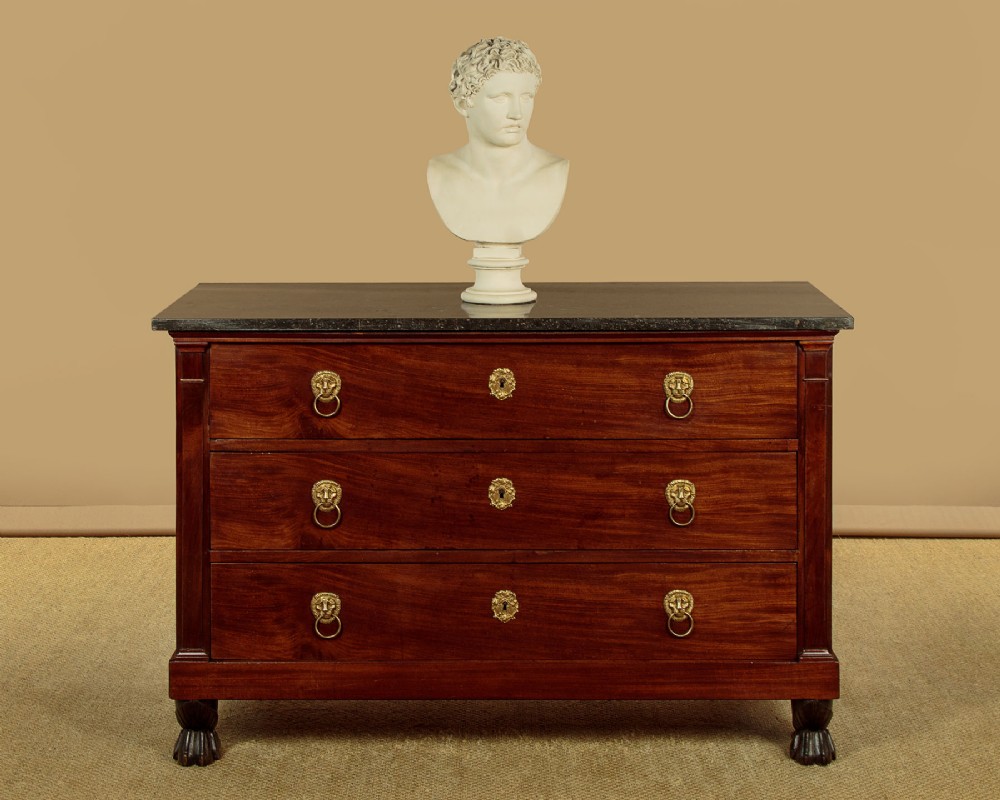 A French Empire mahogany commode featuring three long drawers, brass lion mask ring handles, carved claw feet, and a dark grey marble top. View II