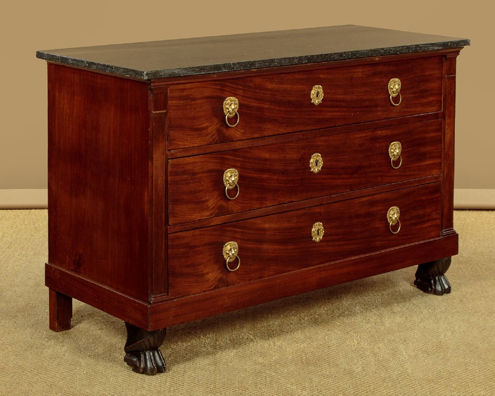 A French Empire mahogany commode featuring three long drawers, brass lion mask ring handles, carved claw feet, and a dark grey marble top. View III