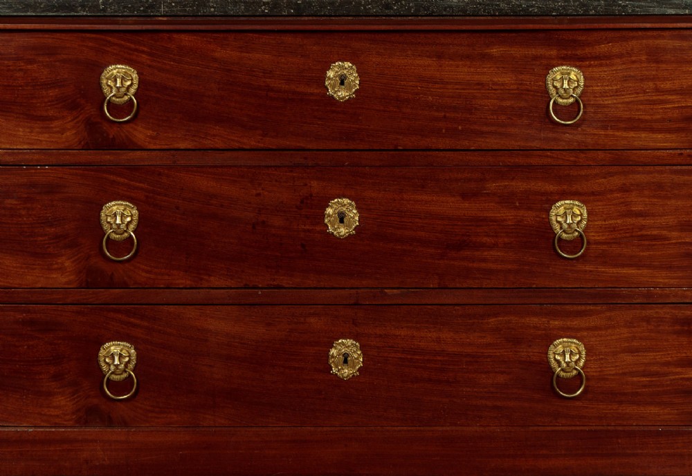 A French Empire mahogany commode featuring three long drawers, brass lion mask ring handles, carved claw feet, and a dark grey marble top. View IX