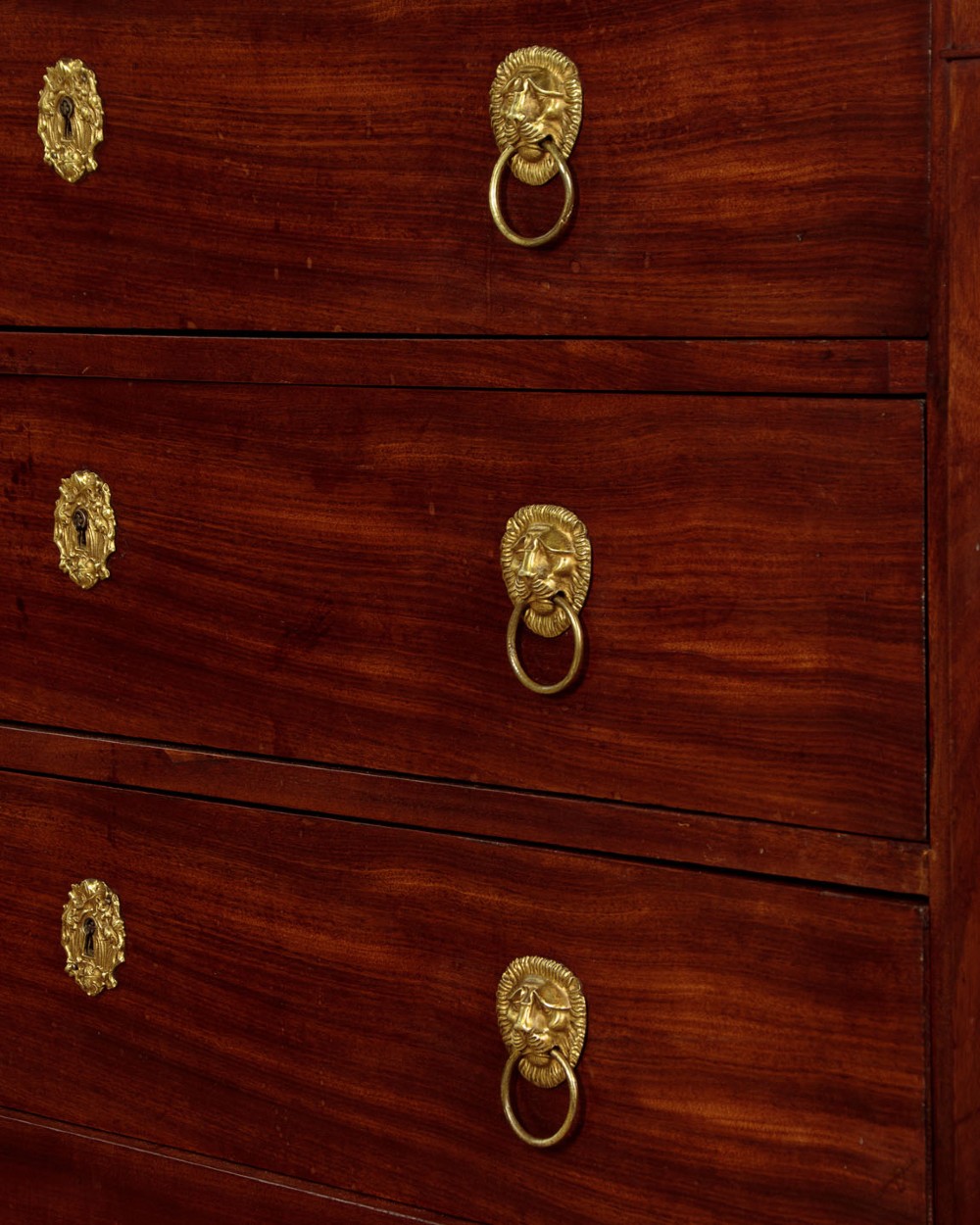 A French Empire mahogany commode featuring three long drawers, brass lion mask ring handles, carved claw feet, and a dark grey marble top. View X