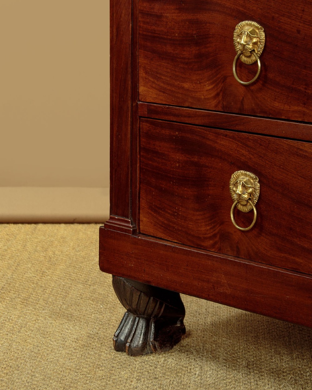 A French Empire mahogany commode featuring three long drawers, brass lion mask ring handles, carved claw feet, and a dark grey marble top. View XIV
