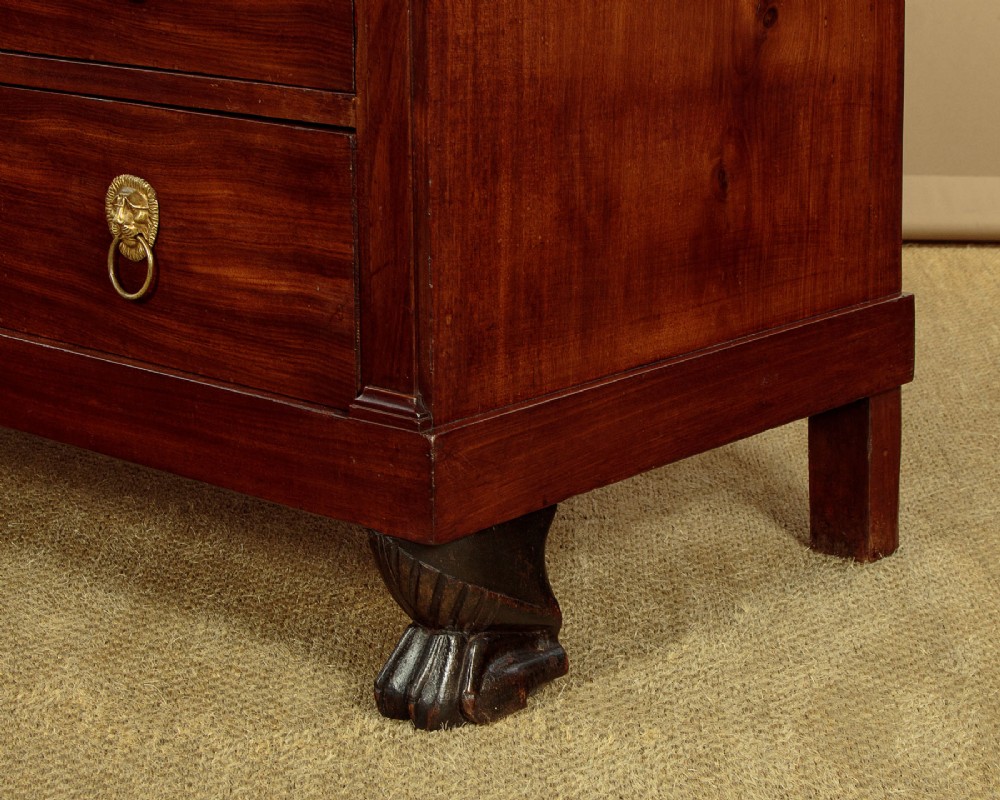 A French Empire mahogany commode featuring three long drawers, brass lion mask ring handles, carved claw feet, and a dark grey marble top. View XV