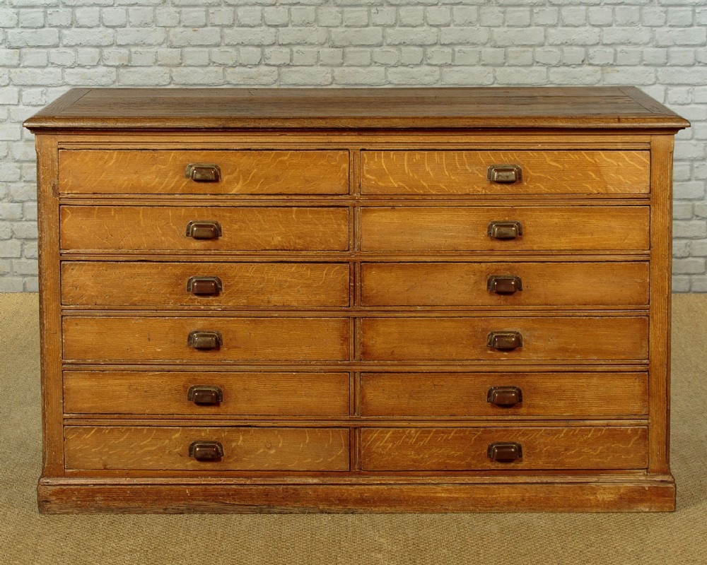 An Edwardian golden oak bank of twelve drawers featuring brass cup handles arranged in two vertical columns.