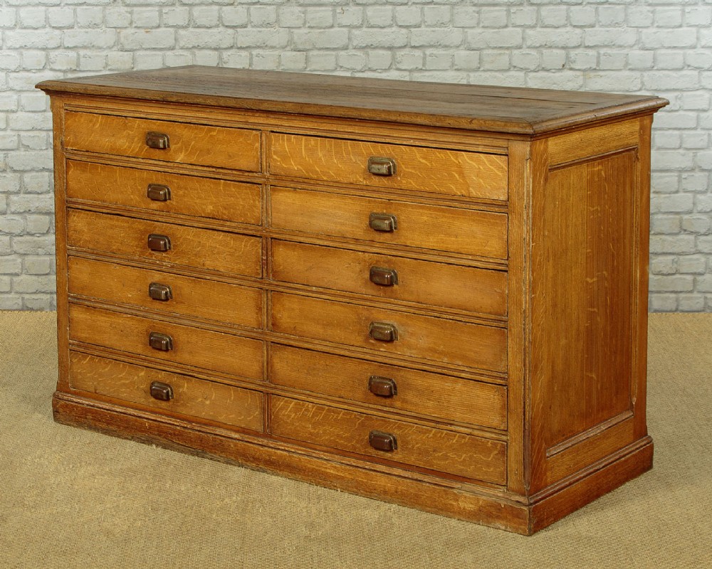 An Edwardian golden oak bank of twelve drawers featuring brass cup handles arranged in two vertical columns. View III