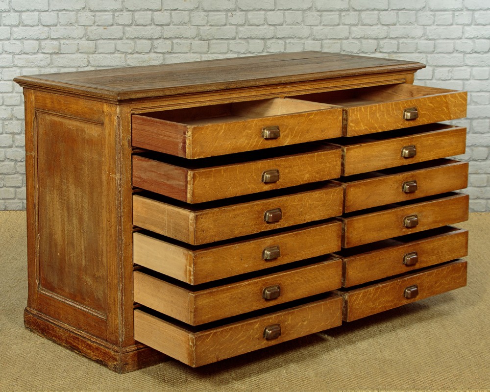 An Edwardian golden oak bank of twelve drawers featuring brass cup handles arranged in two vertical columns. View IV
