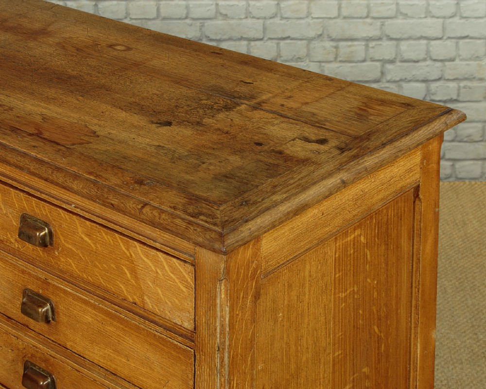 An Edwardian golden oak bank of twelve drawers featuring brass cup handles arranged in two vertical columns. View VI