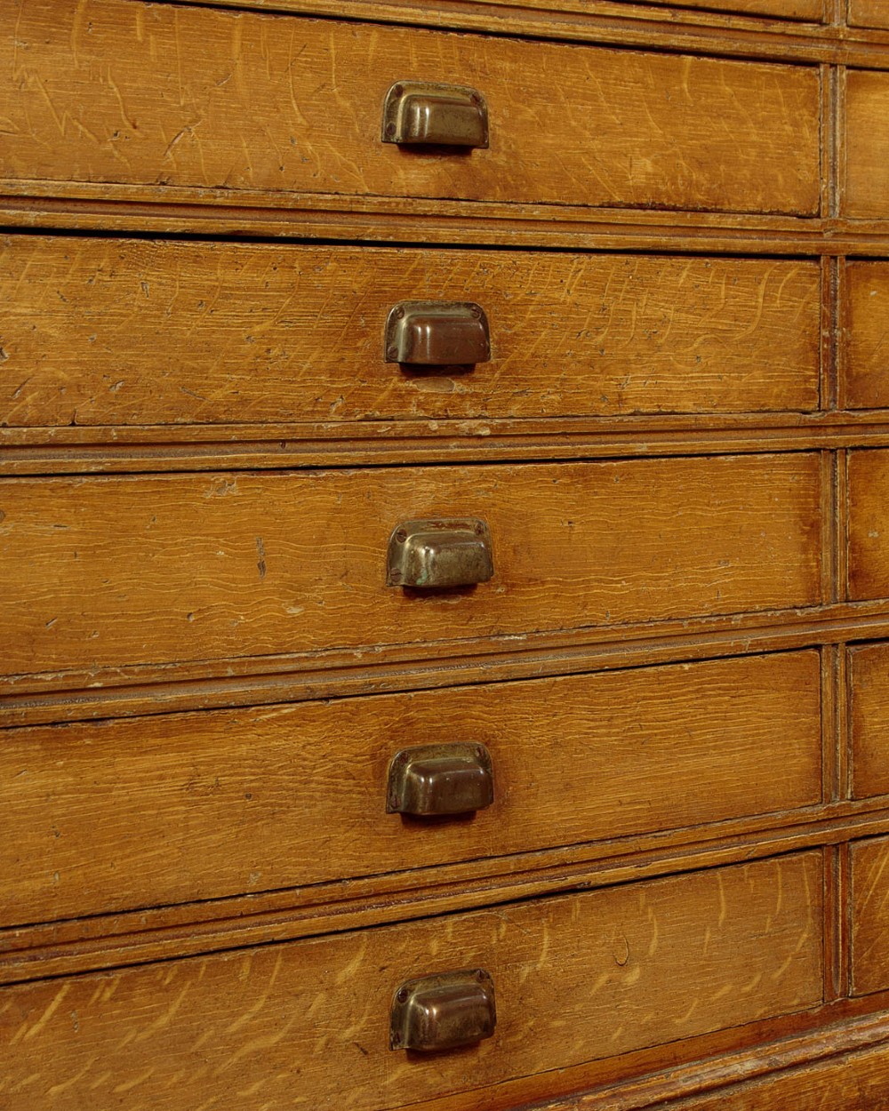 An Edwardian golden oak bank of twelve drawers featuring brass cup handles arranged in two vertical columns. View VIII