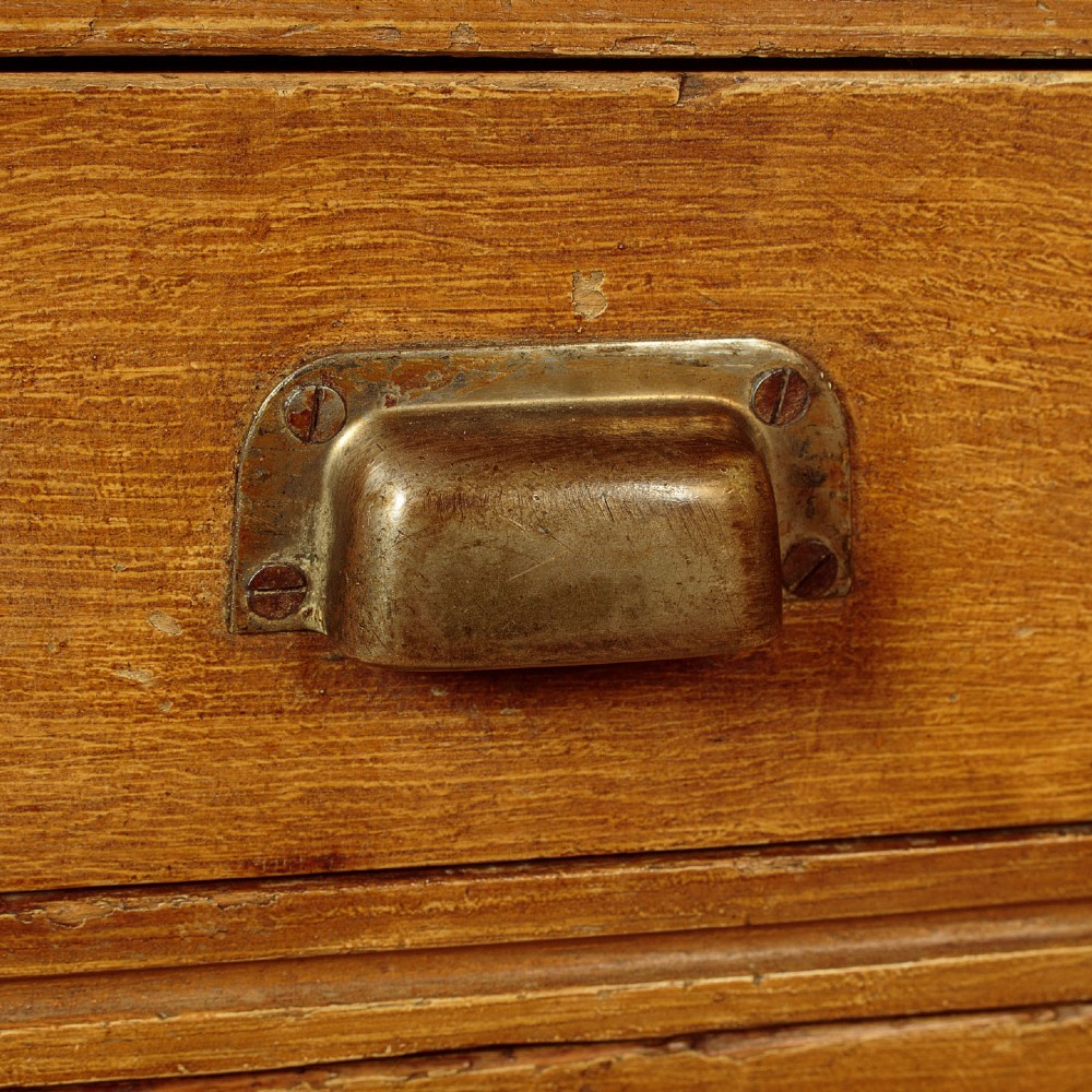 An Edwardian golden oak bank of twelve drawers featuring brass cup handles arranged in two vertical columns. View IX