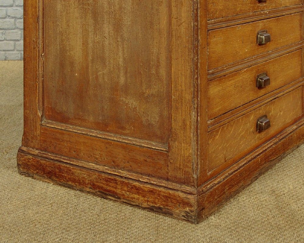 An Edwardian golden oak bank of twelve drawers featuring brass cup handles arranged in two vertical columns. View X