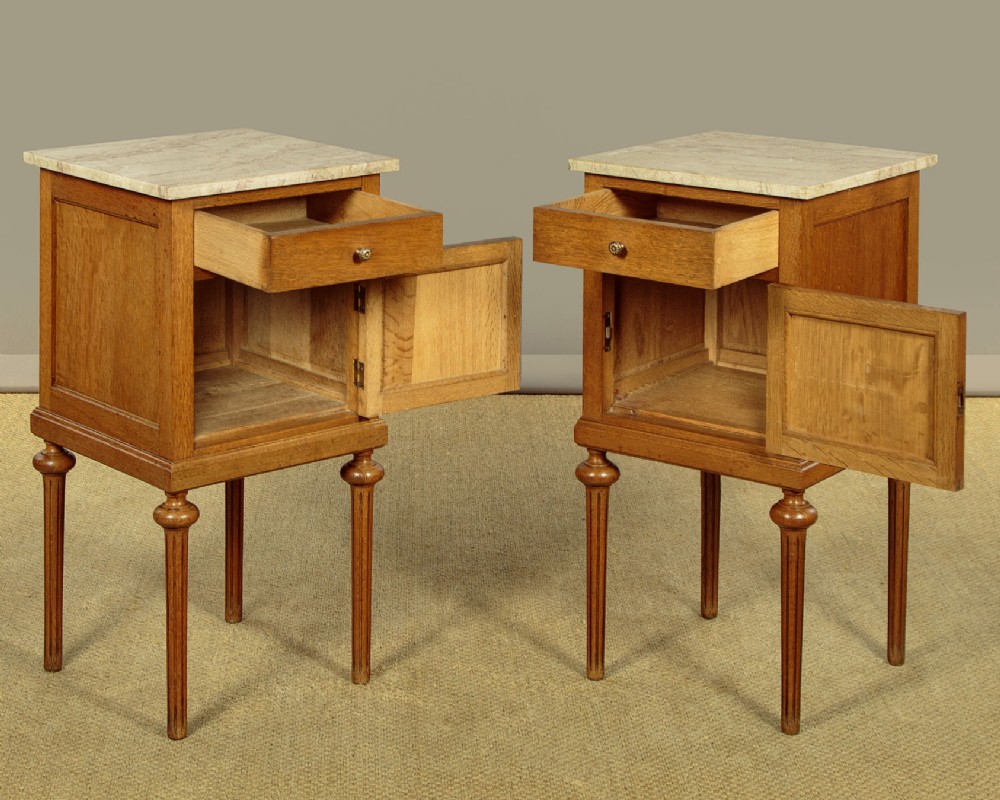A pair of golden oak bedside cabinets featuring marble tops, single drawers, floral carved cupboard doors, and slim fluted turned legs. View II