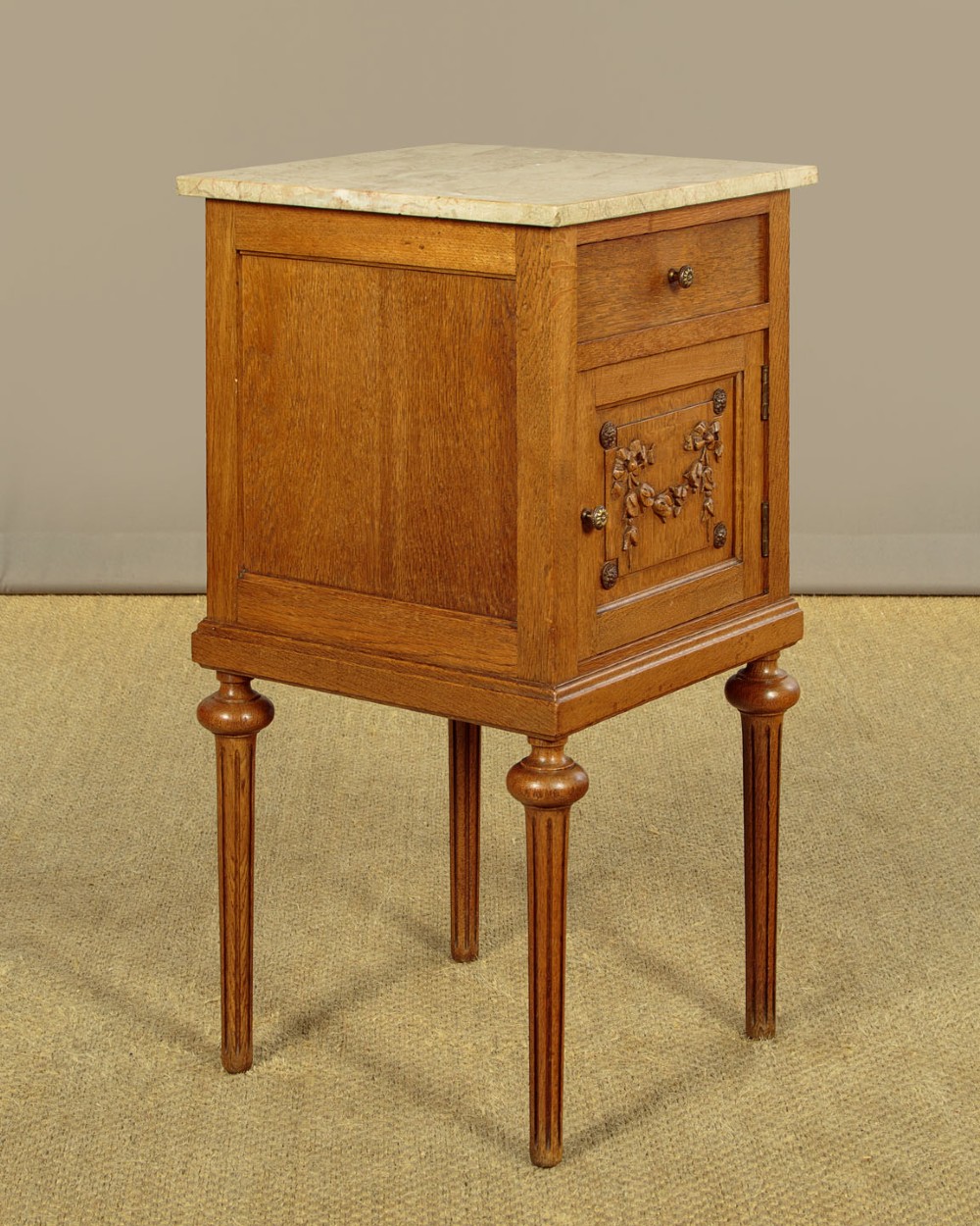 A pair of golden oak bedside cabinets featuring marble tops, single drawers, floral carved cupboard doors, and slim fluted turned legs. View V
