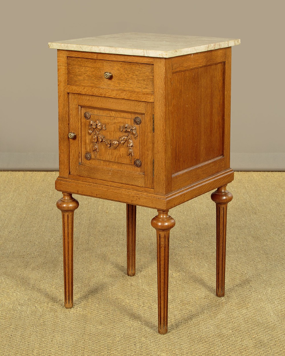 A pair of golden oak bedside cabinets featuring marble tops, single drawers, floral carved cupboard doors, and slim fluted turned legs. View VI