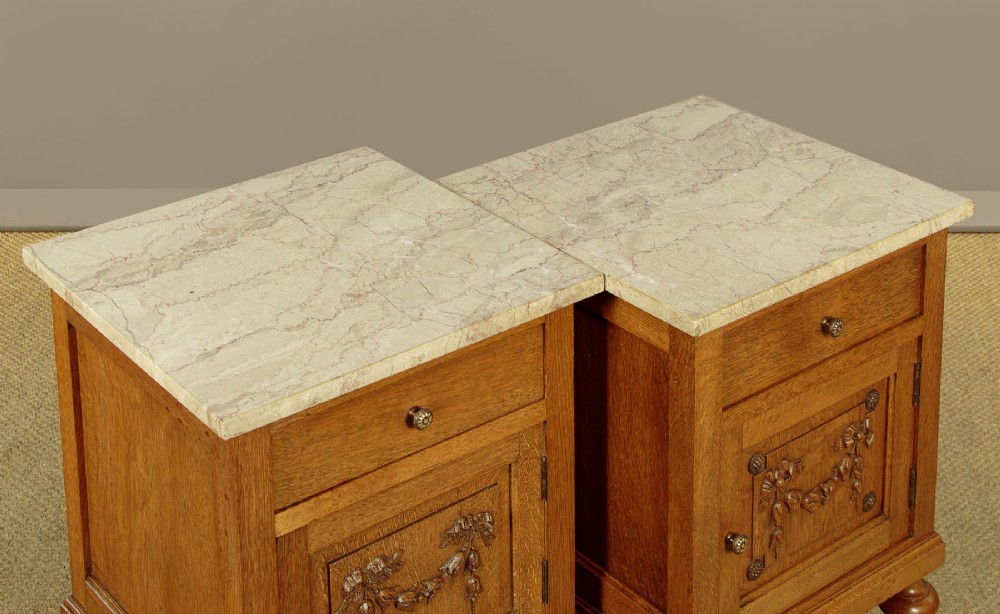A pair of golden oak bedside cabinets featuring marble tops, single drawers, floral carved cupboard doors, and slim fluted turned legs. View VII