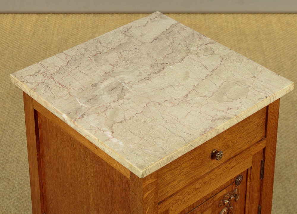 A pair of golden oak bedside cabinets featuring marble tops, single drawers, floral carved cupboard doors, and slim fluted turned legs. View VIII
