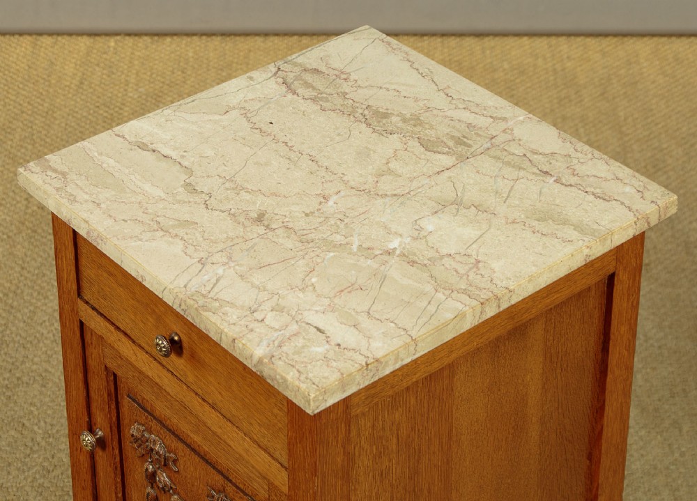 A pair of golden oak bedside cabinets featuring marble tops, single drawers, floral carved cupboard doors, and slim fluted turned legs. View IX