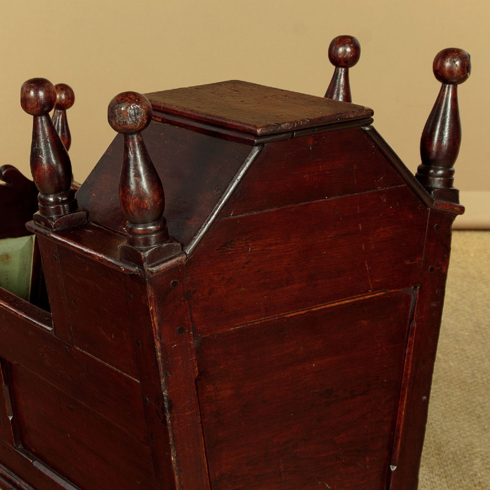 An antique dark brown wooden hooded rocking cradle featuring turned corner finials, a curved rocker base, and a pale green painted interior. View IV