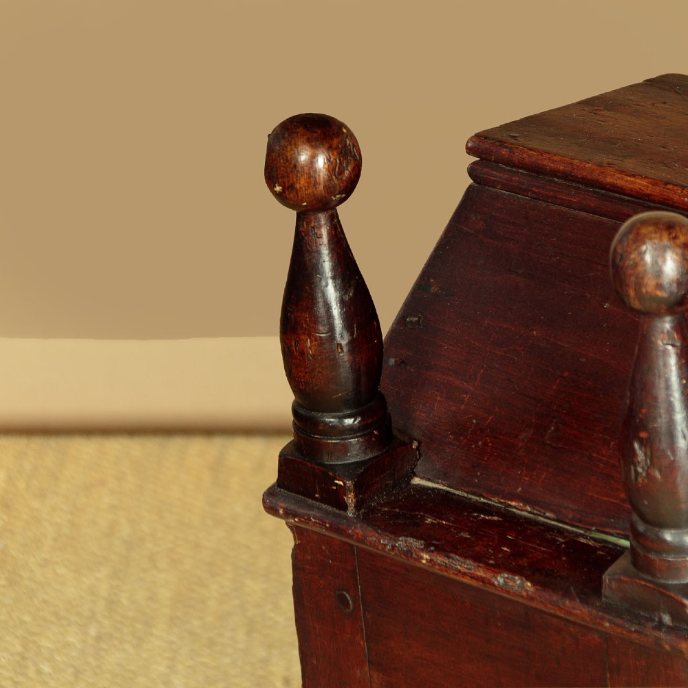 An antique dark brown wooden hooded rocking cradle featuring turned corner finials, a curved rocker base, and a pale green painted interior. View V