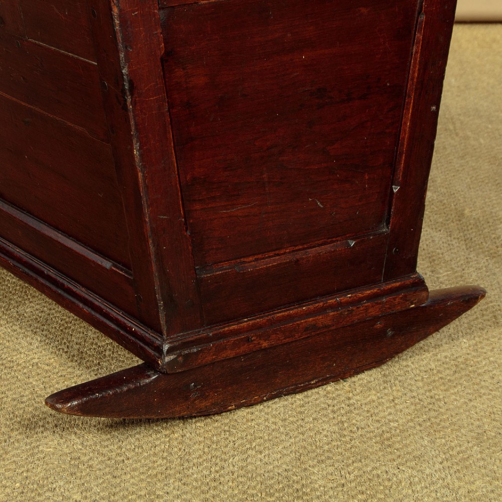 An antique dark brown wooden hooded rocking cradle featuring turned corner finials, a curved rocker base, and a pale green painted interior. View IX