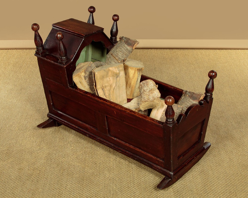 An antique dark brown wooden hooded rocking cradle featuring turned corner finials, a curved rocker base, and a pale green painted interior. View X