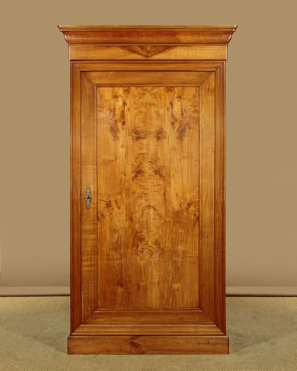 A single-door antique French Louis Philippe cherrywood wardrobe with figured timber grain and a moulded cornice.
