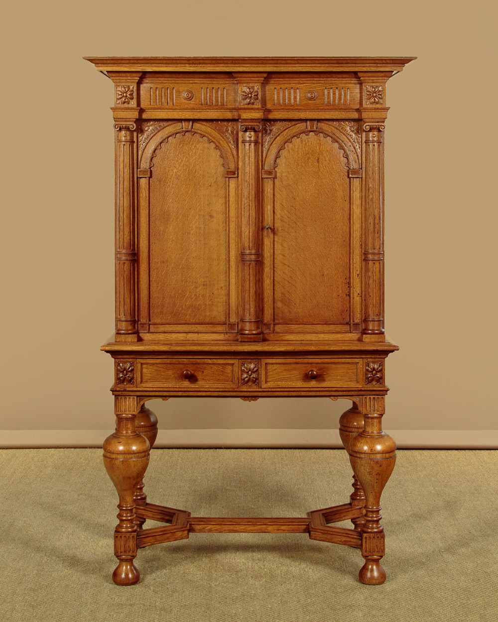 A warm brown oak cabinet featuring arched doors set upon a matching stand with large turned bulbous legs and lower stretchers. View II
