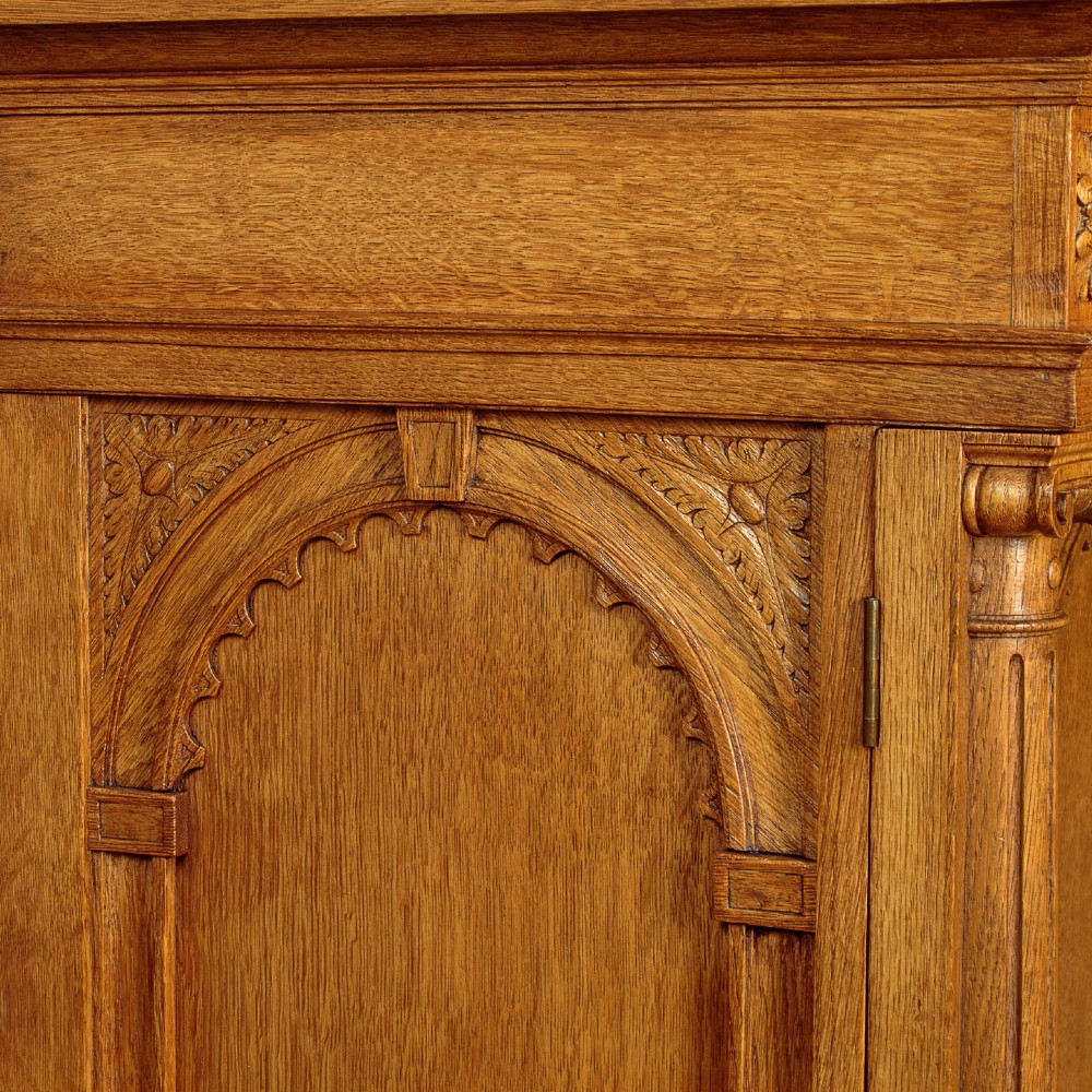 A warm brown oak cabinet featuring arched doors set upon a matching stand with large turned bulbous legs and lower stretchers. View VI