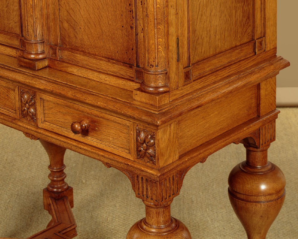 A warm brown oak cabinet featuring arched doors set upon a matching stand with large turned bulbous legs and lower stretchers. View IX