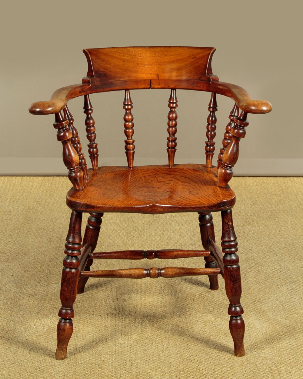 A Victorian smokers bow wooden armchair with turned spindles, a curved top rail, a contoured elm seat, and turned legs.
