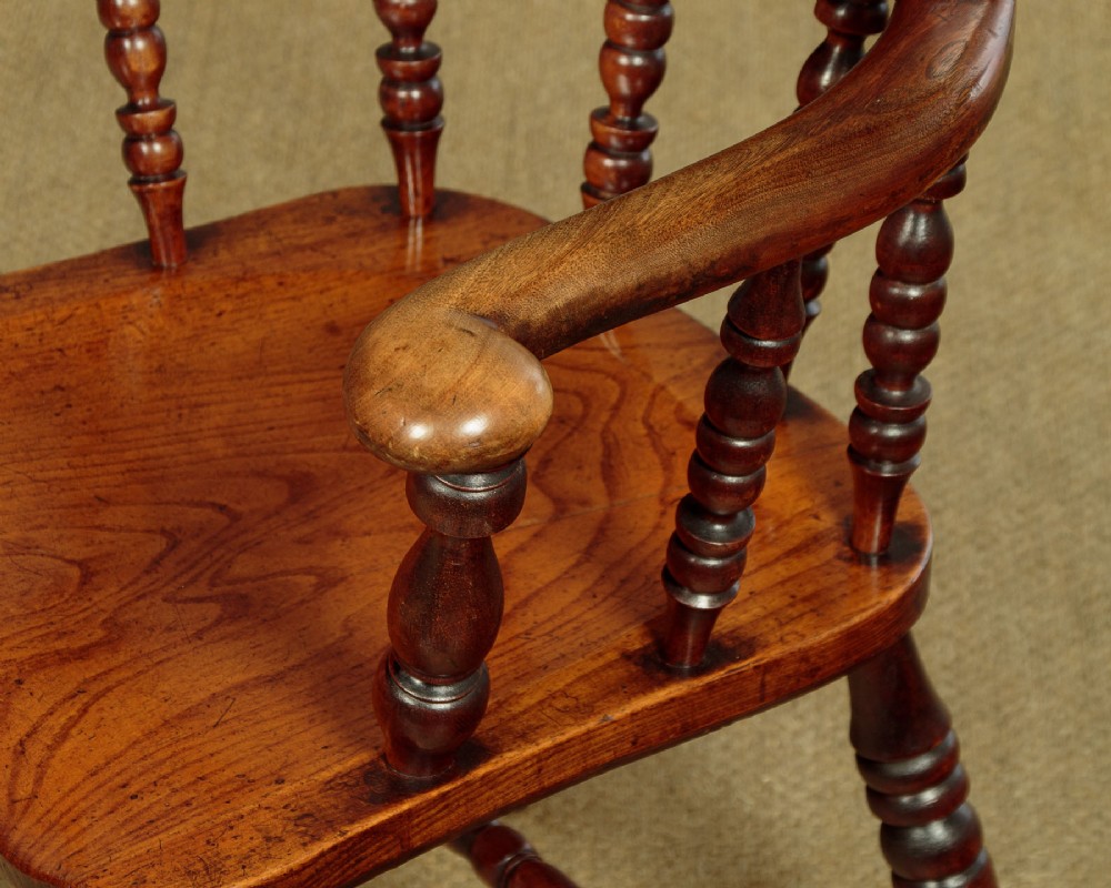A Victorian smokers bow wooden armchair with turned spindles, a curved top rail, a contoured elm seat, and turned legs. View VII