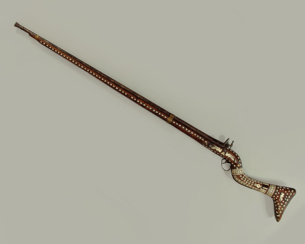 An antique Afghan Jezail musket featuring a distinctly curved wooden stock decorated with geometric bone inlay and a steel lock mechanism. View II